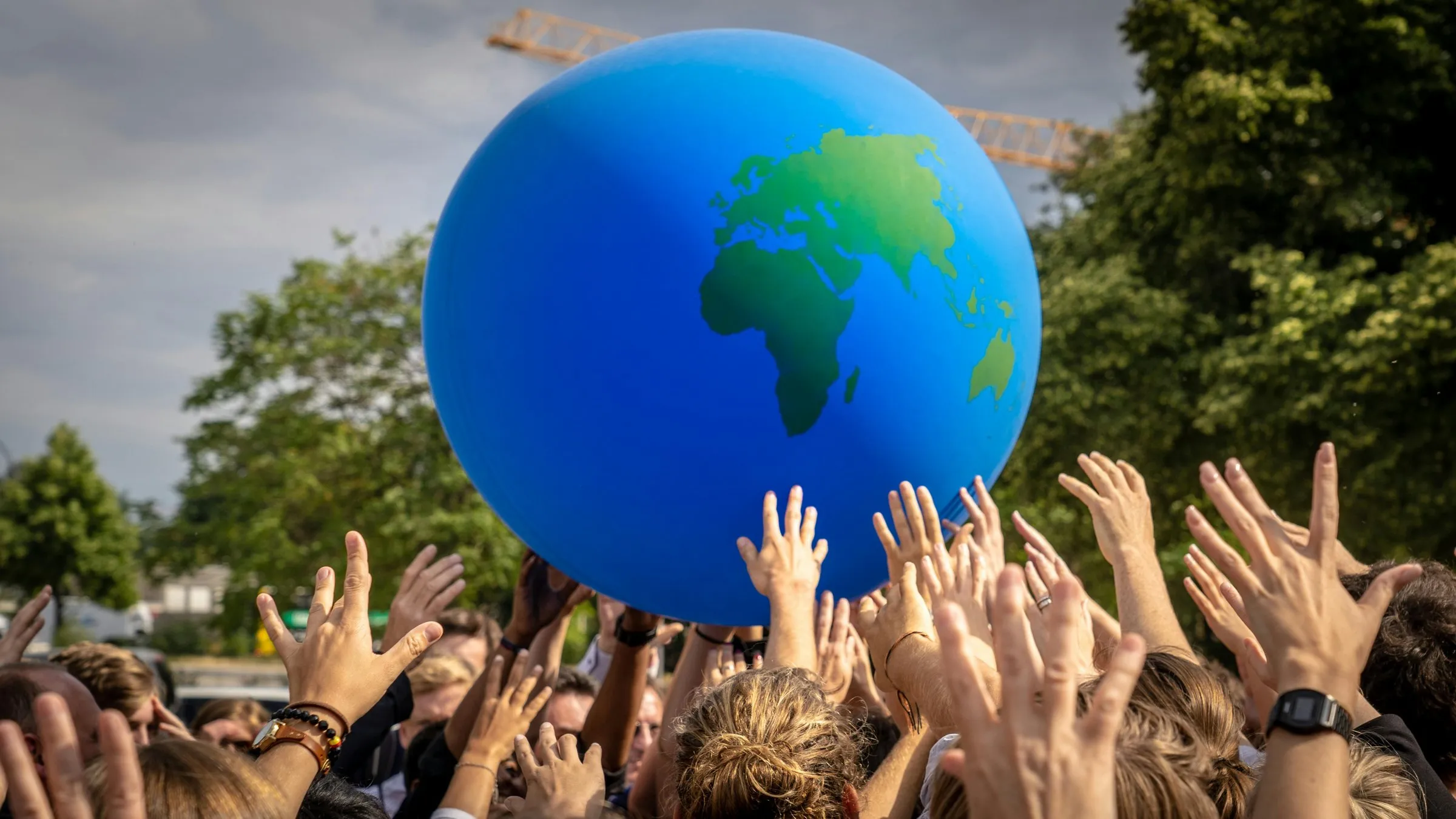 People raising their hands toward a large inflatable globe at a public event in Berlin.